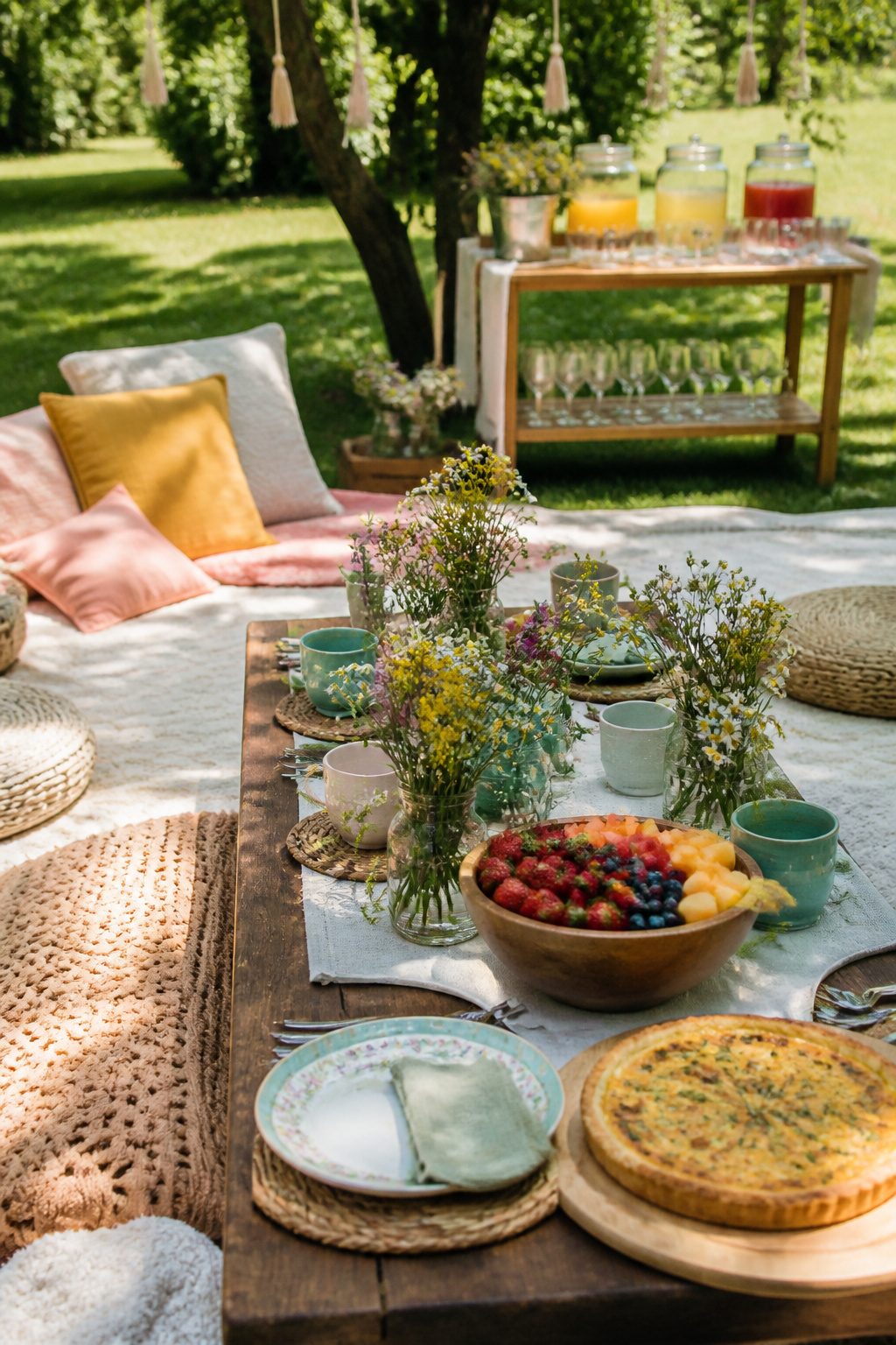 Colorful picnic brunch setup with quiche and fresh fruit on blankets.