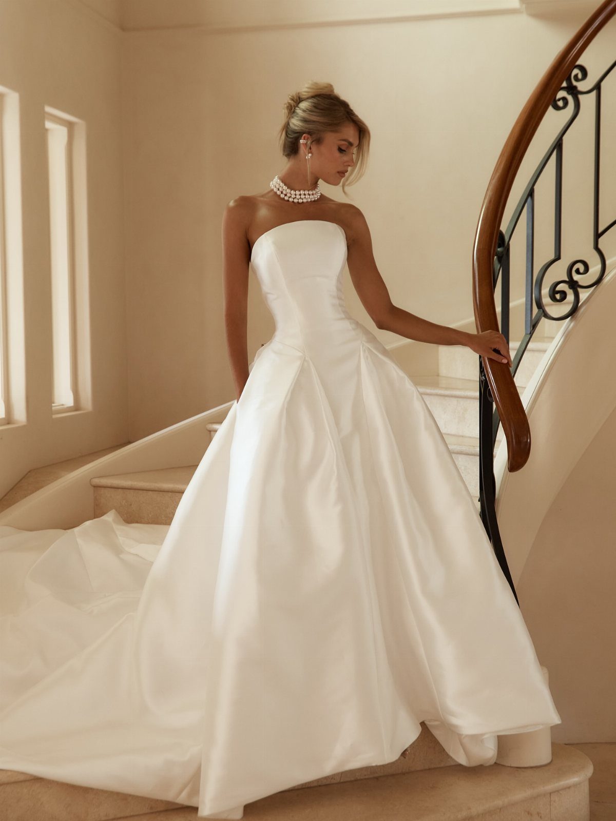 Woman in a white strapless satin wedding dress posing on an elegant staircase.