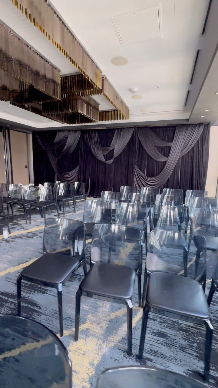 Black fabric drapery swaged elegantly against a wall in an event space with clear chairs.