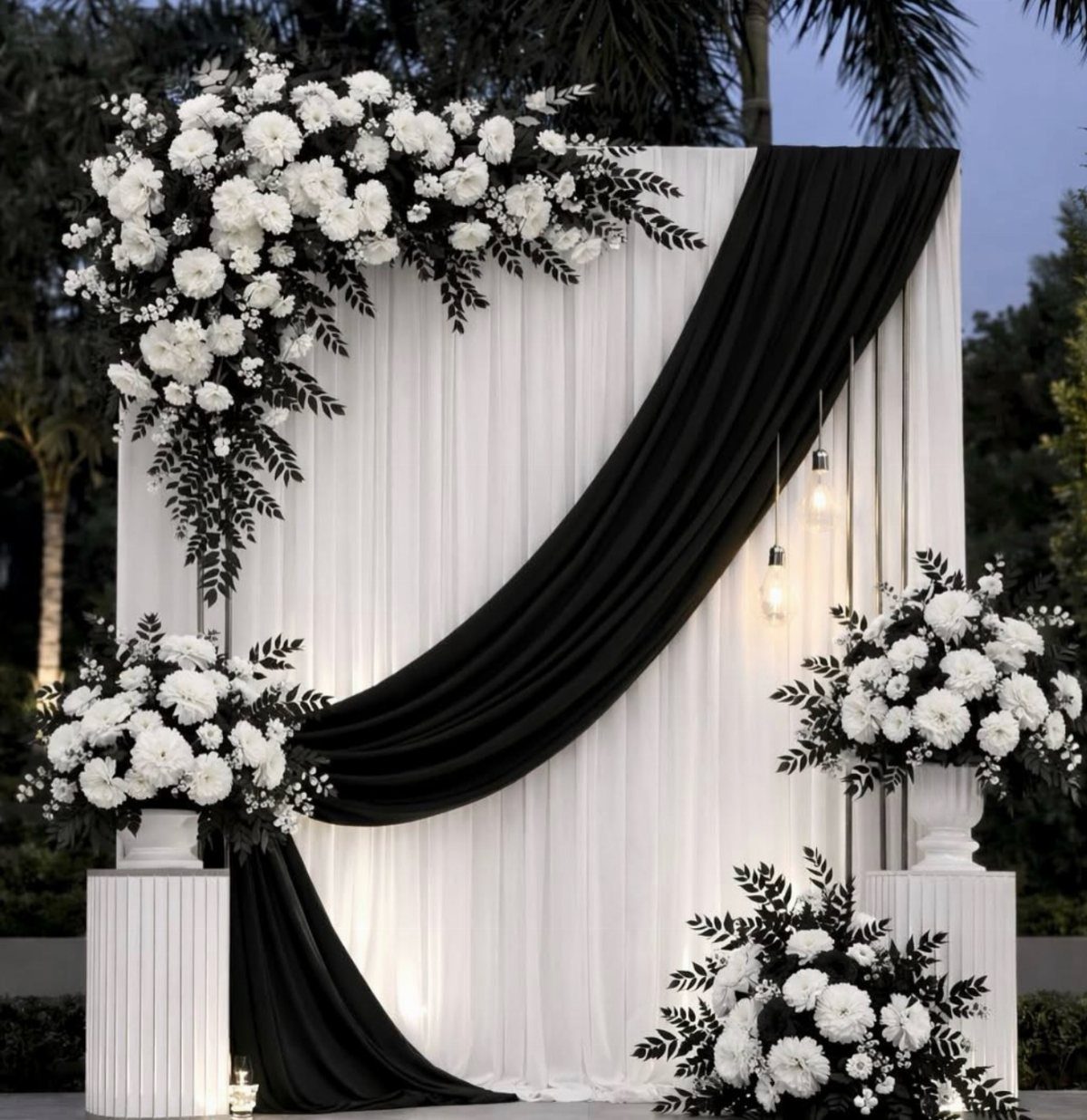 White drapery backdrop with black fabric swoop and white floral arrangements on pedestals.