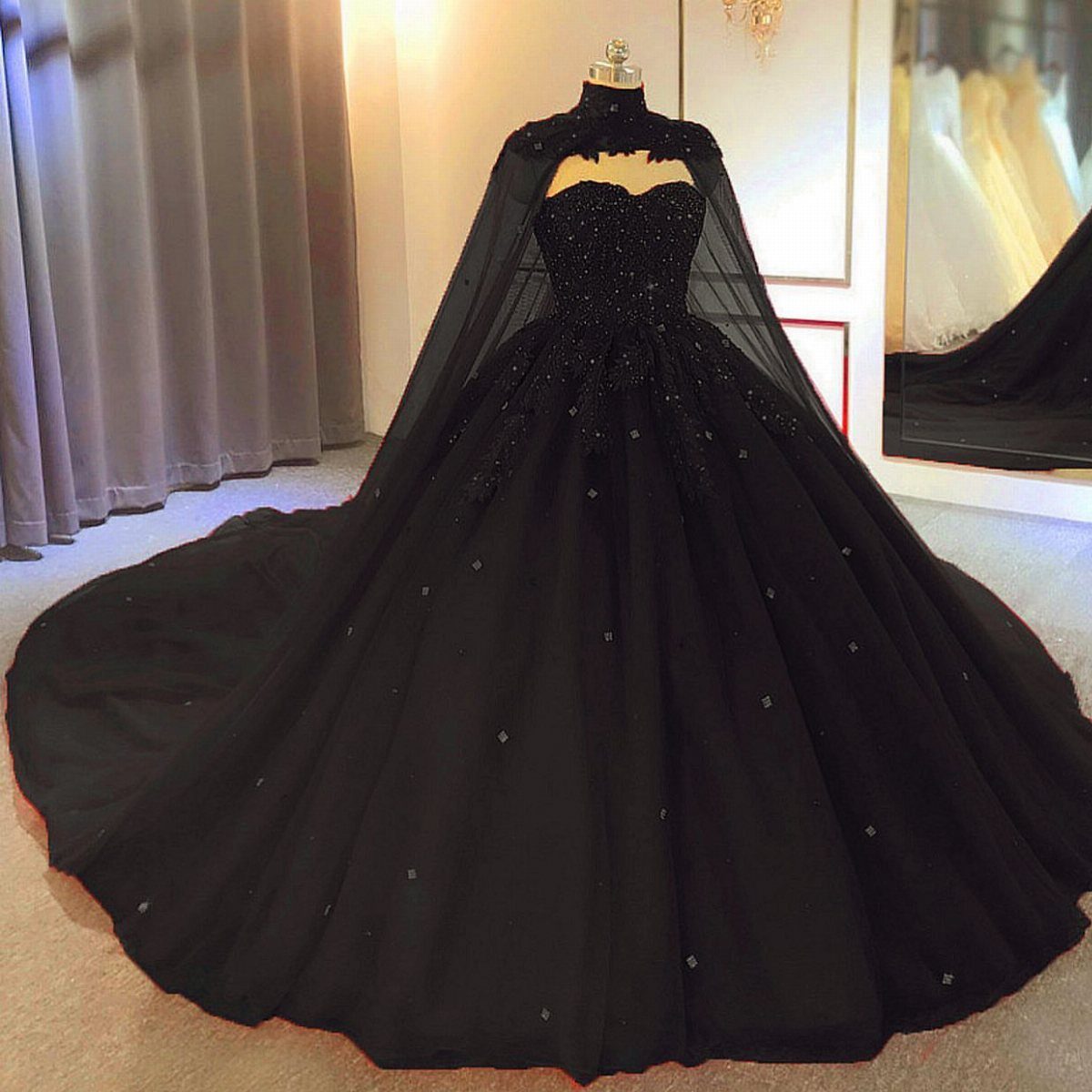 A black beaded wedding gown with a sheer cape displayed on a mannequin.