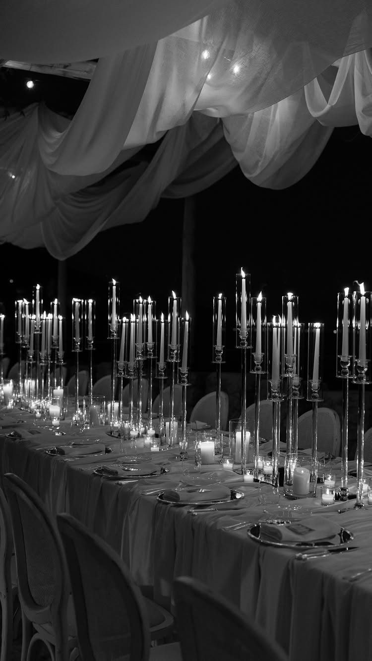 Tall taper candles and small votives illuminate a long, elegantly set wedding reception table.