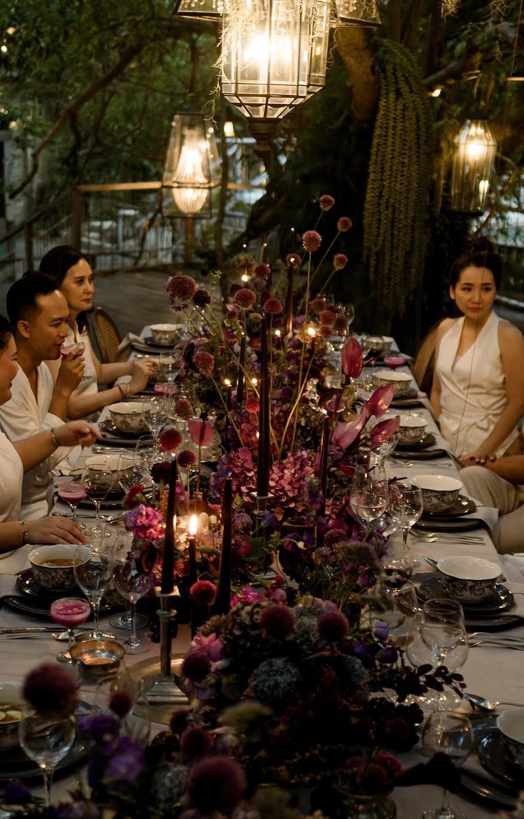 Dark purple and pink floral arrangements with black taper candles on a long dining table.