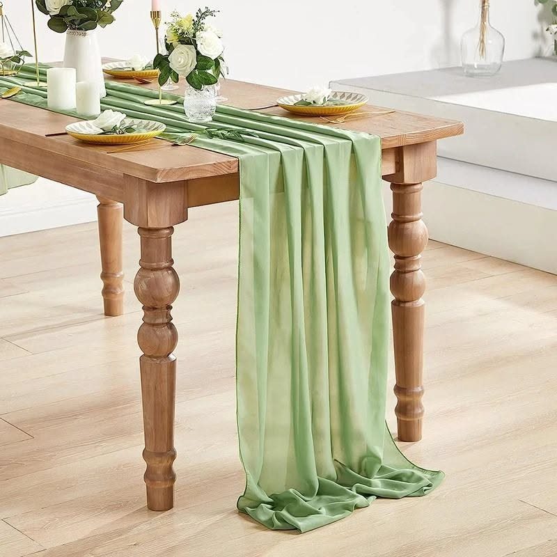 21 Colorful Wedding Table Settings for Every Style and Budget 14 A light green chiffon runner draped over a wooden table with floral arrangements and candles.