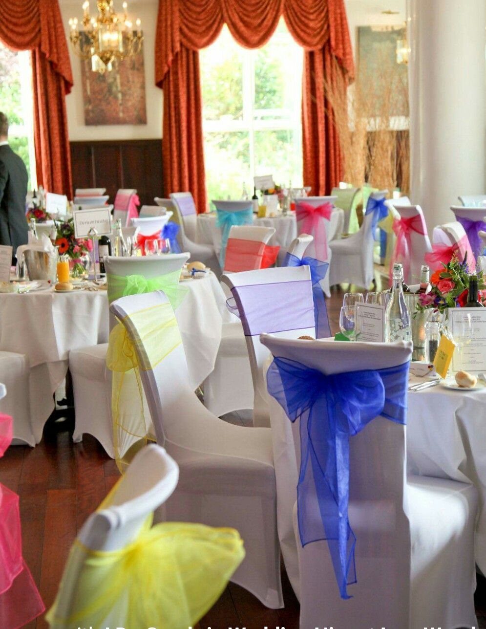 21 Colorful Wedding Table Settings for Every Style and Budget 19 White chairs decorated with colorful sheer fabric sashes in a wedding reception setting.