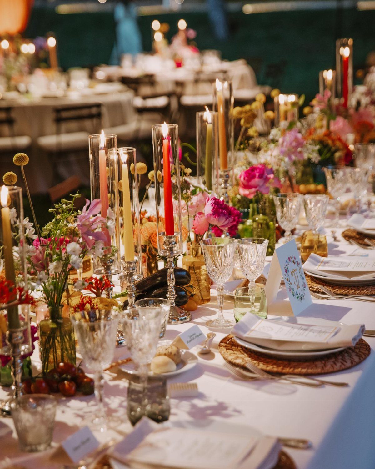 21 Colorful Wedding Table Settings for Every Style and Budget 4 Colorful taper candles in glass holders arranged on a decorated wedding table with flowers.