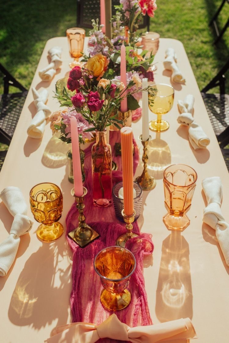 21 Colorful Wedding Table Settings for Every Style and Budget 20 An outdoor table set with colorful glassware, taper candles, and bright floral arrangements on a magenta runner.