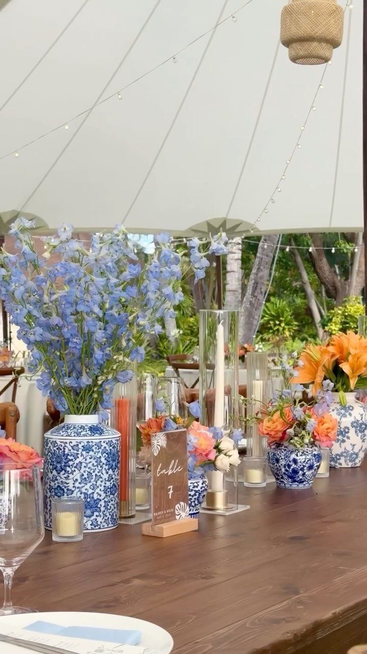 21 Colorful Wedding Table Settings for Every Style and Budget 8 Blue and white patterned ceramic vases and clear glass cylinder vases filled with flowers and candles on a wooden table.