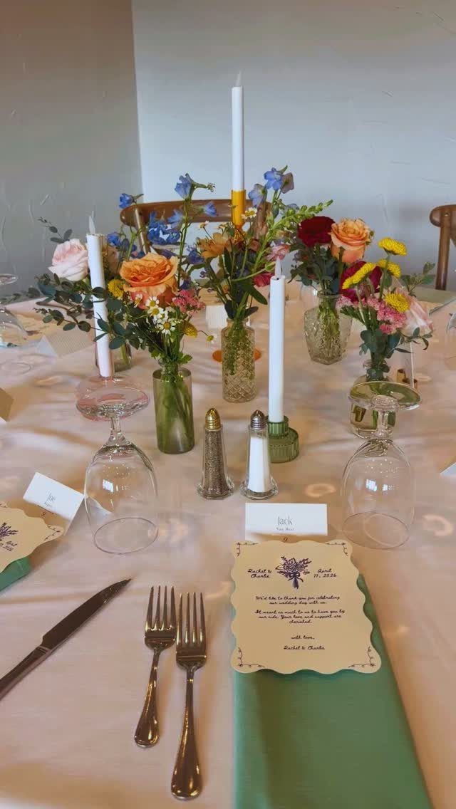 21 Colorful Wedding Table Settings for Every Style and Budget 18 A formal table setting with green napkins, silver cutlery, and colorful floral arrangements in glass vases.