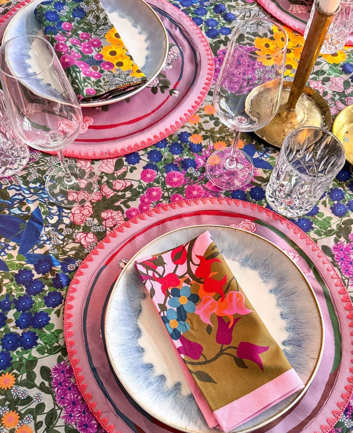 21 Colorful Wedding Table Settings for Every Style and Budget 11 Floral patterned napkins placed on plates atop a colorful floral tablecloth with pink chargers and glassware.