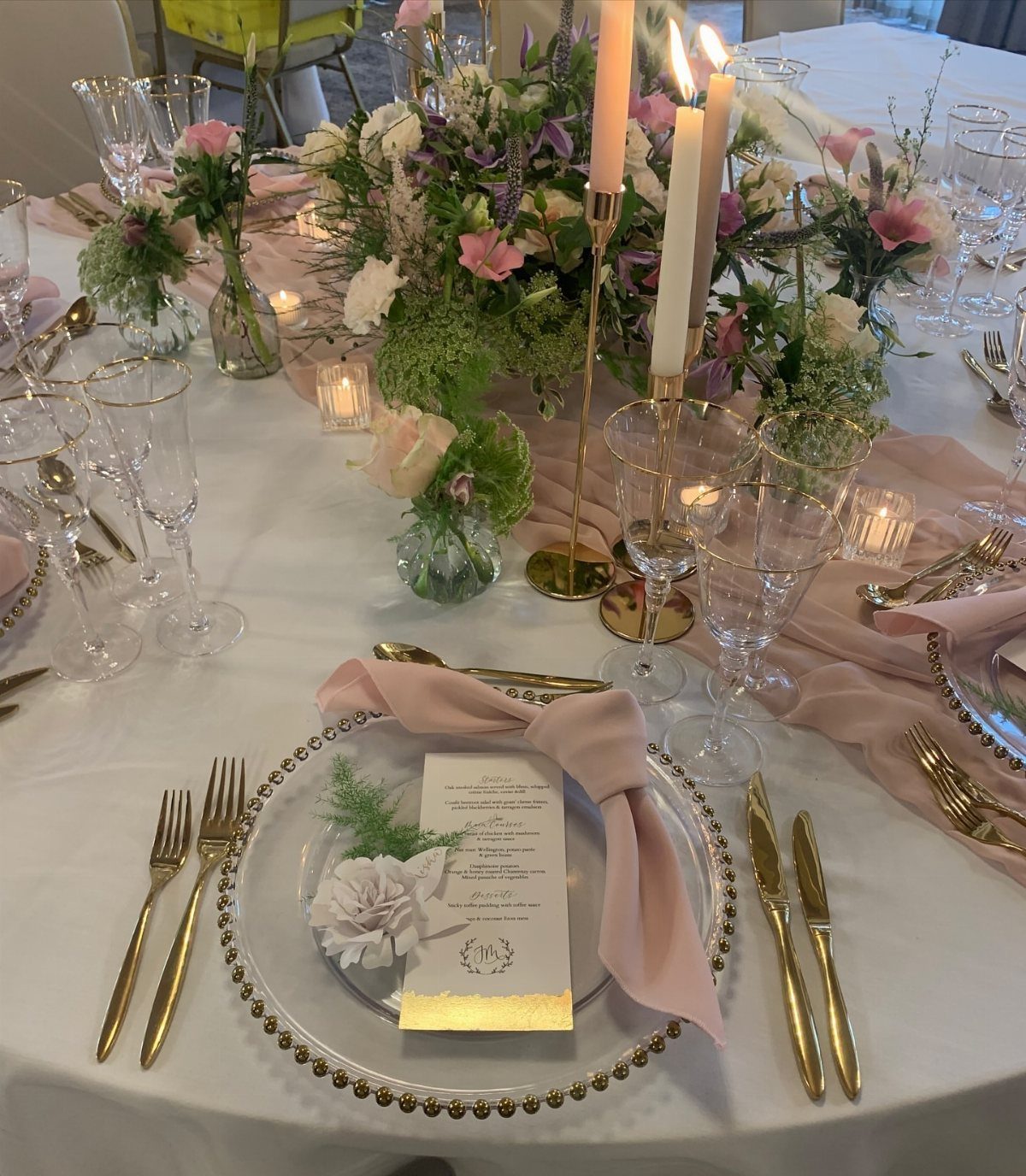 21 Colorful Wedding Table Settings for Every Style and Budget 16 Elegant wedding table setting with gold cutlery, pink linens, floral arrangements, and gold taper candle holders.