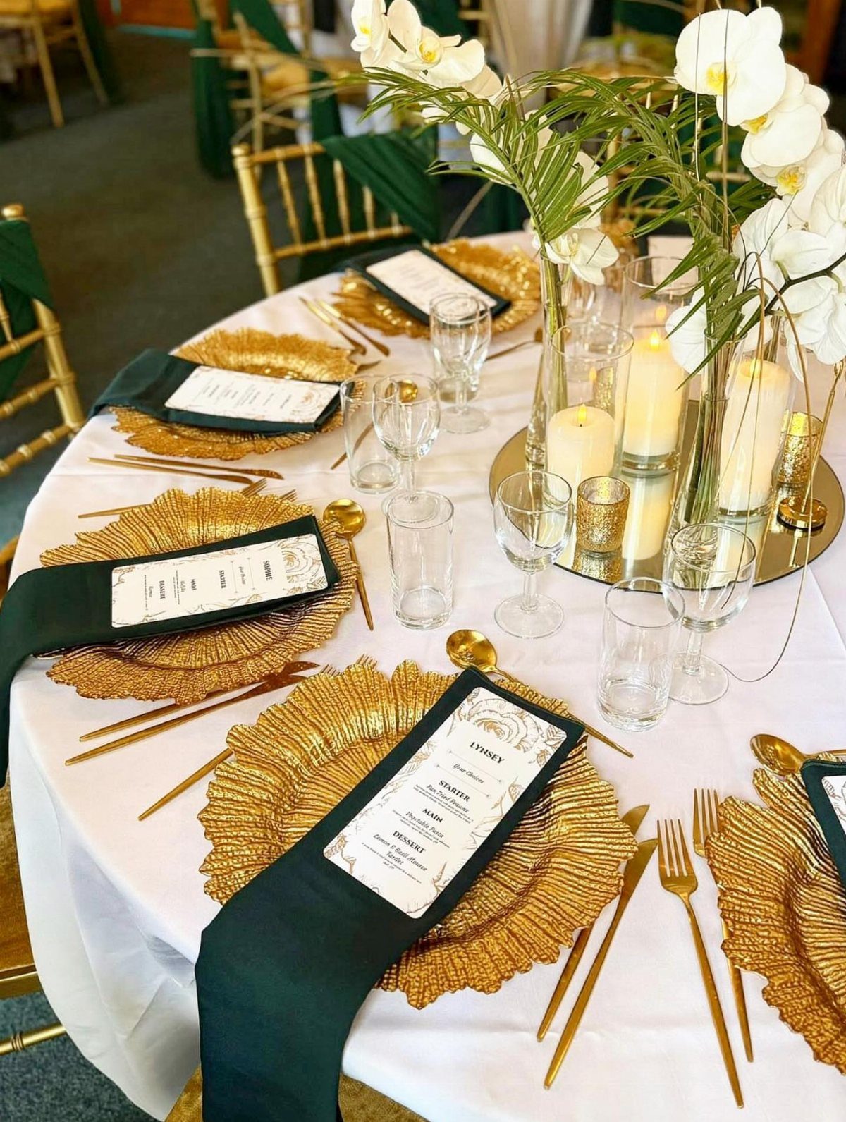 21 Colorful Wedding Table Settings for Every Style and Budget 6 A wedding table setting featuring gold chargers, gold cutlery, green napkins, and white orchid centerpieces.
