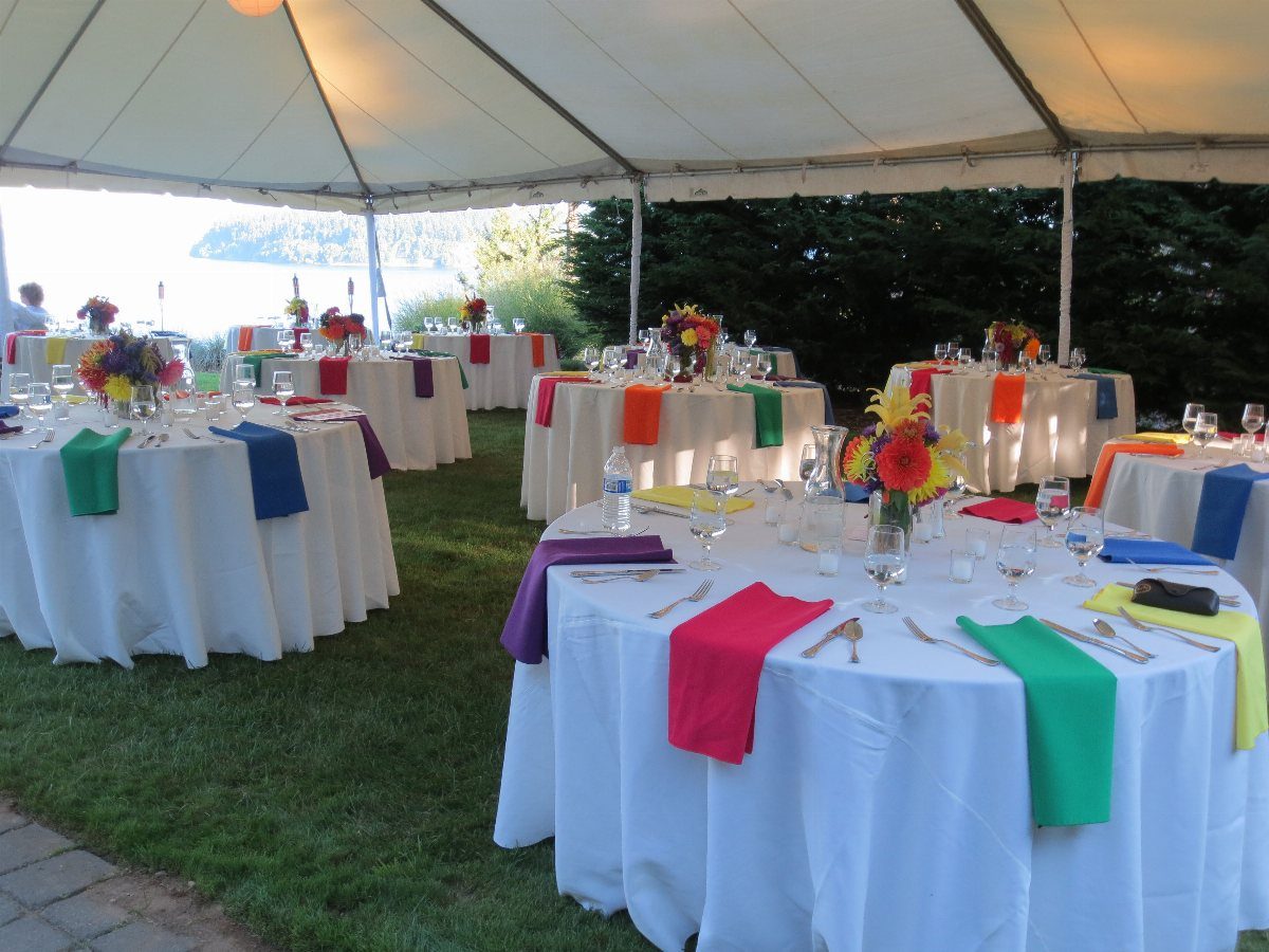 21 Colorful Wedding Table Settings for Every Style and Budget 3 Round tables with white linens and vibrant, multi-colored napkins set under a large outdoor tent.