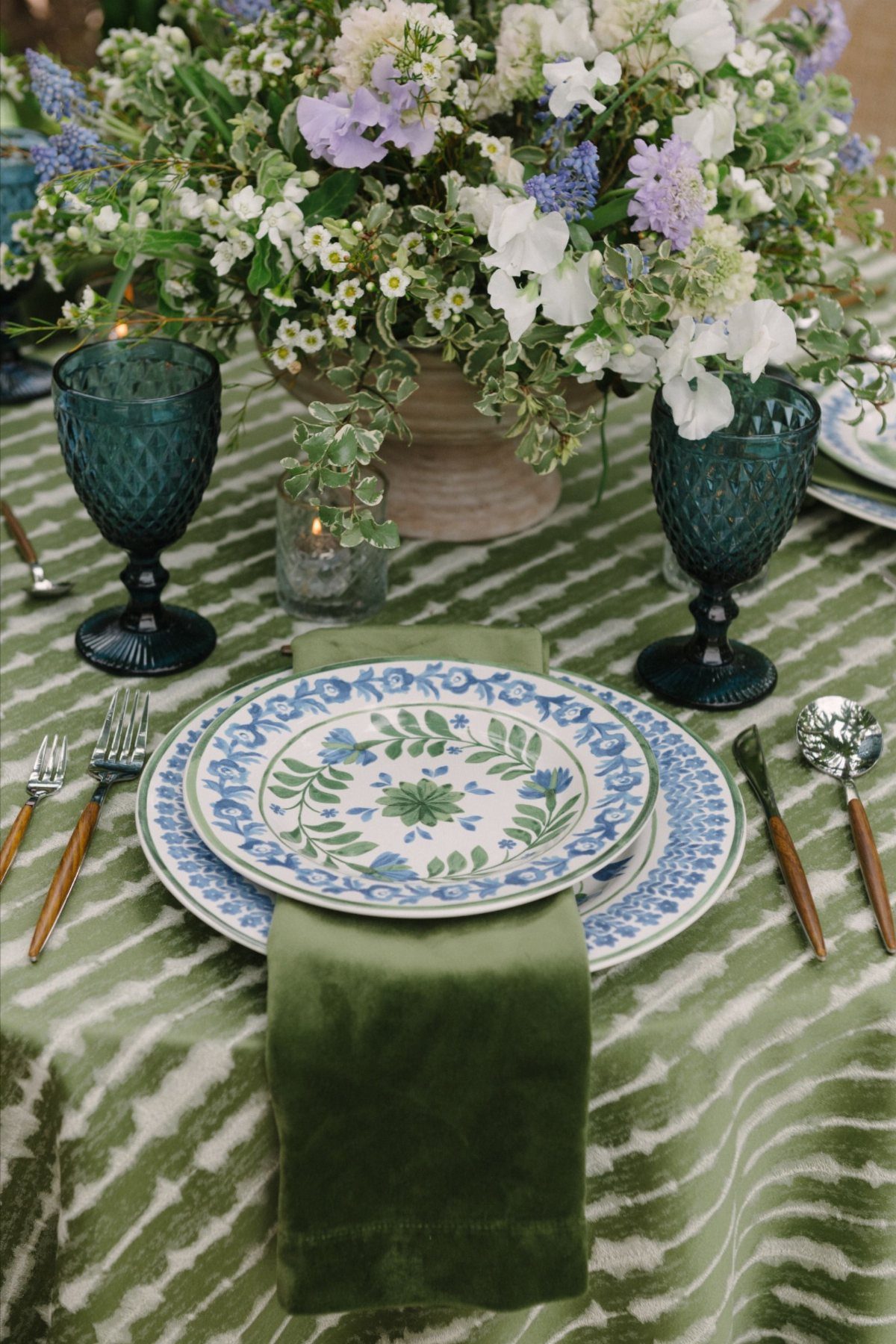 21 Colorful Wedding Table Settings for Every Style and Budget 5 A table setting with green patterned tablecloth, floral plates, teal glasses, and wildflower centerpiece.