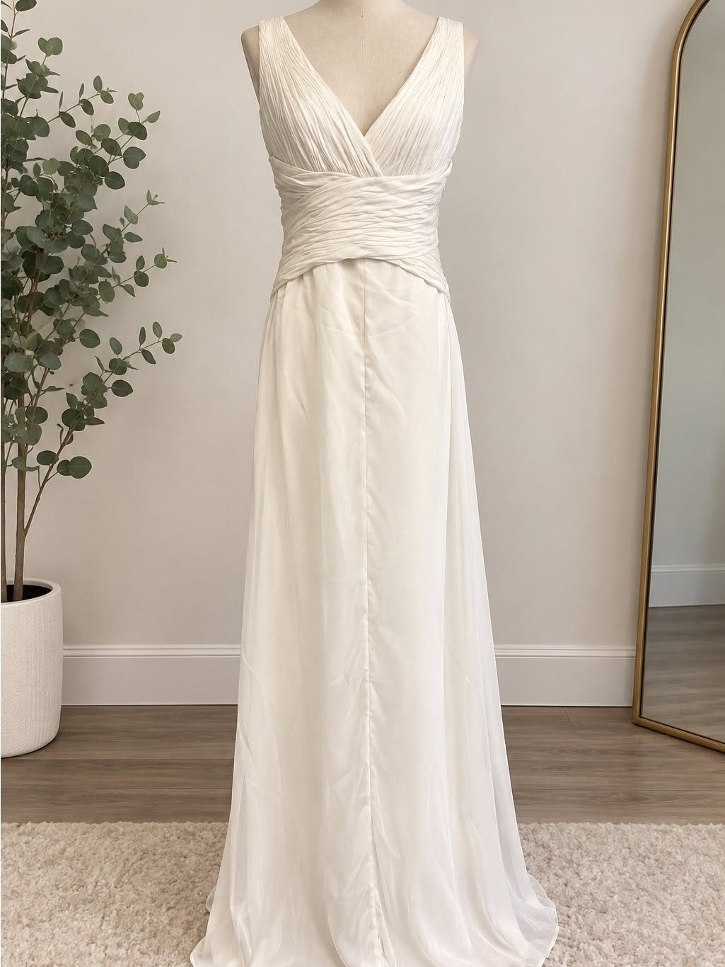 Cream white sleeveless wedding dress with a pleated bodice and flowing skirt on a mannequin.
