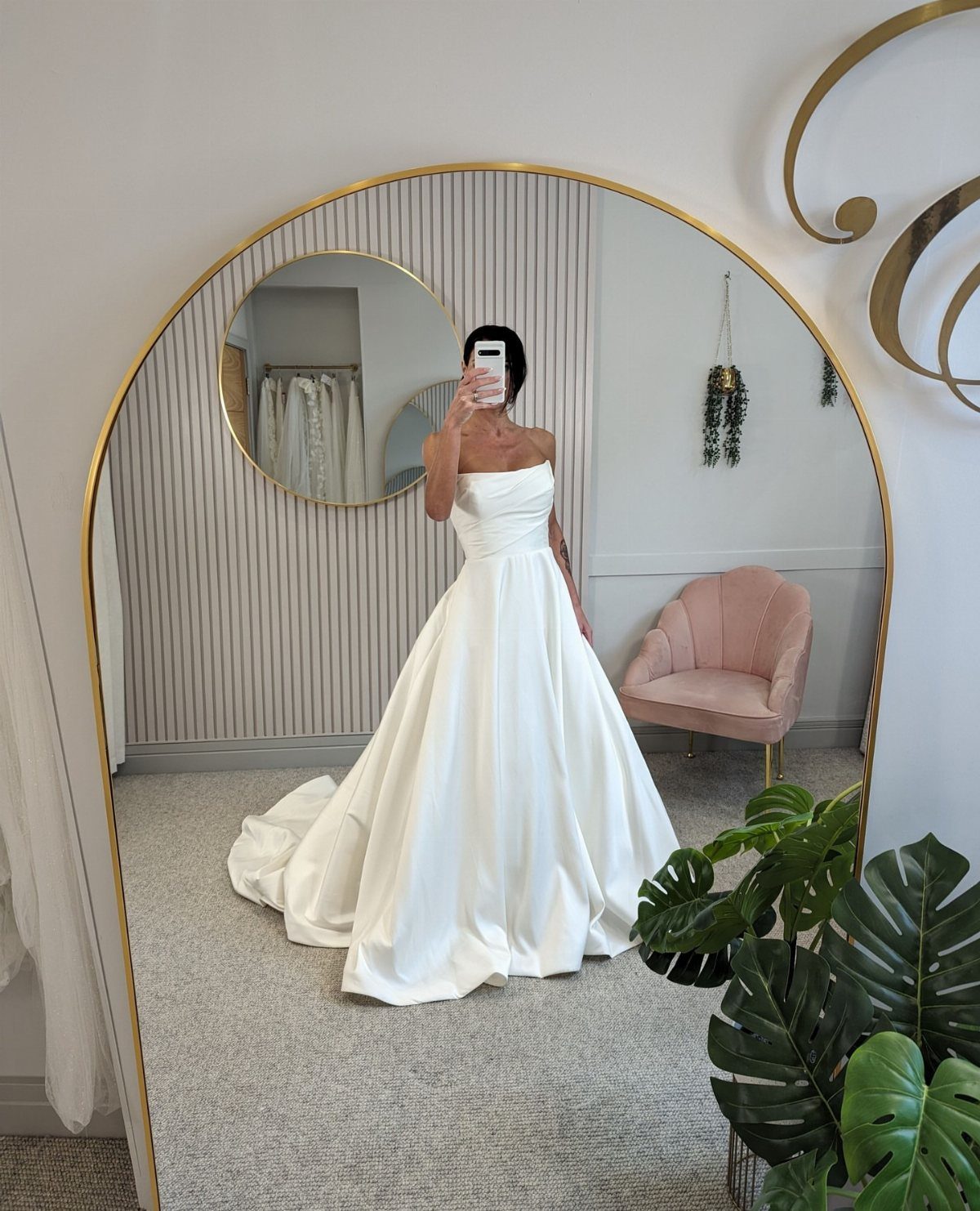 A woman in a strapless cream white satin A-line wedding dress posing for a mirror selfie.
