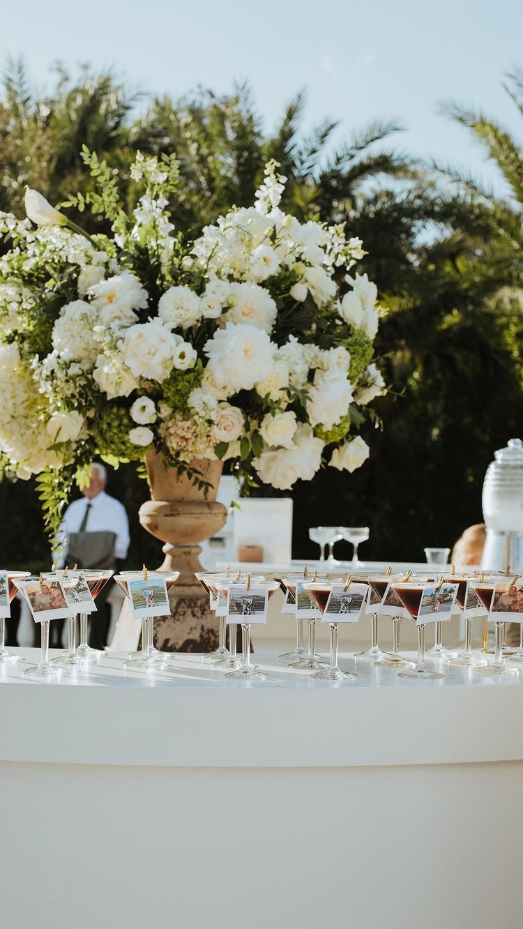 13 Cute and Fun Wedding Ideas for Guests Your Guests Will Love 10 White floral arrangement and small glasses with attached photos on a white table outdoors.