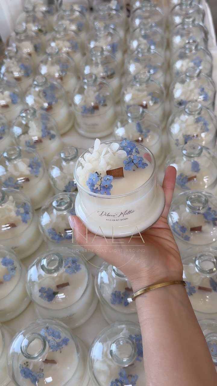 13 Cute and Fun Wedding Ideas for Guests Your Guests Will Love 6 A hand holding a small decorative glass jar candle with white and blue flowers.