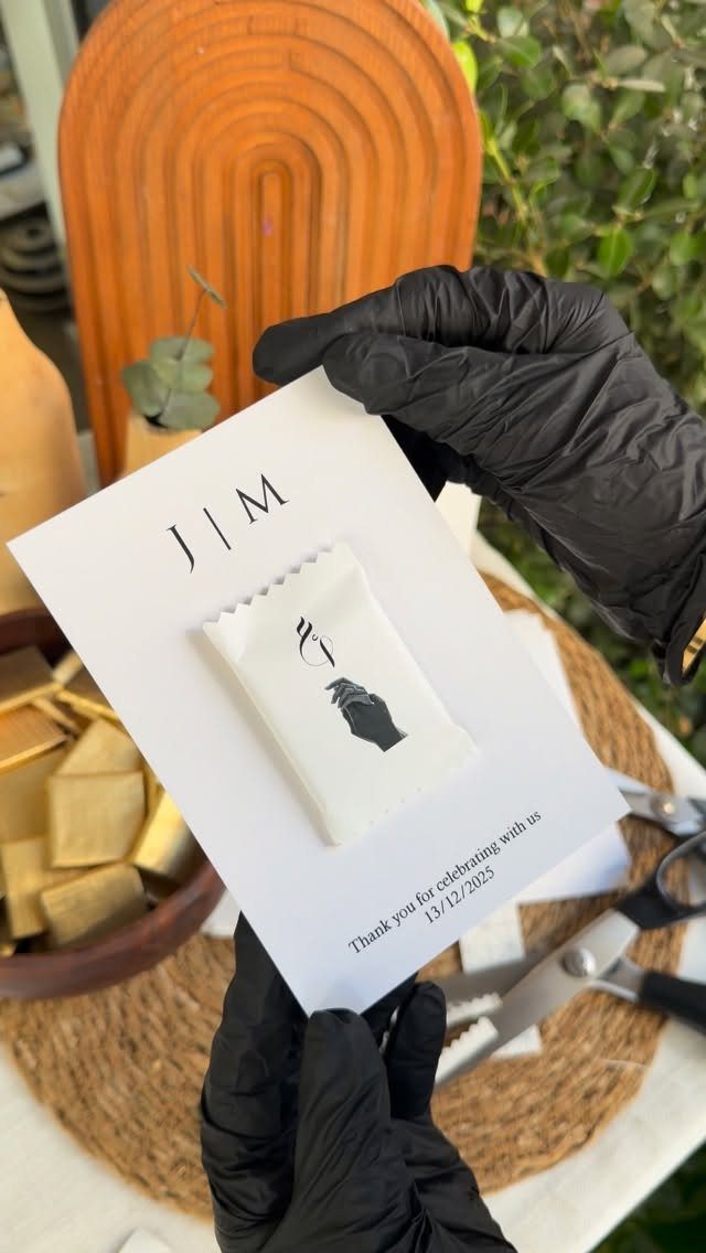 13 Cute and Fun Wedding Ideas for Guests Your Guests Will Love 2 Hands in black gloves holding a personalized white chocolate bar on a custom card.
