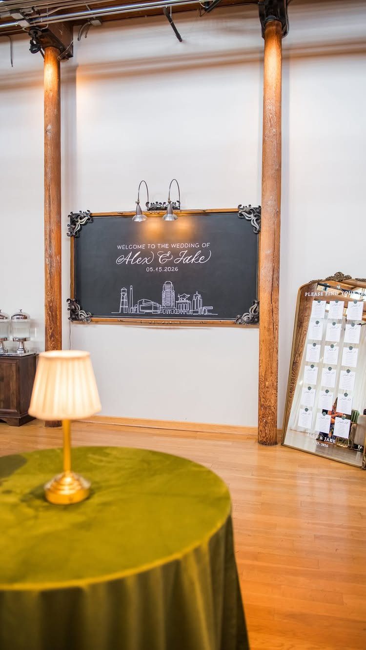 A large chalkboard wedding welcome sign hanging on a white wall between wooden pillars.