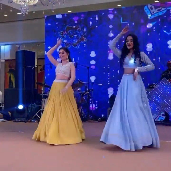 Two women in colorful traditional Indian attire performing a choreographed dance on a stage.