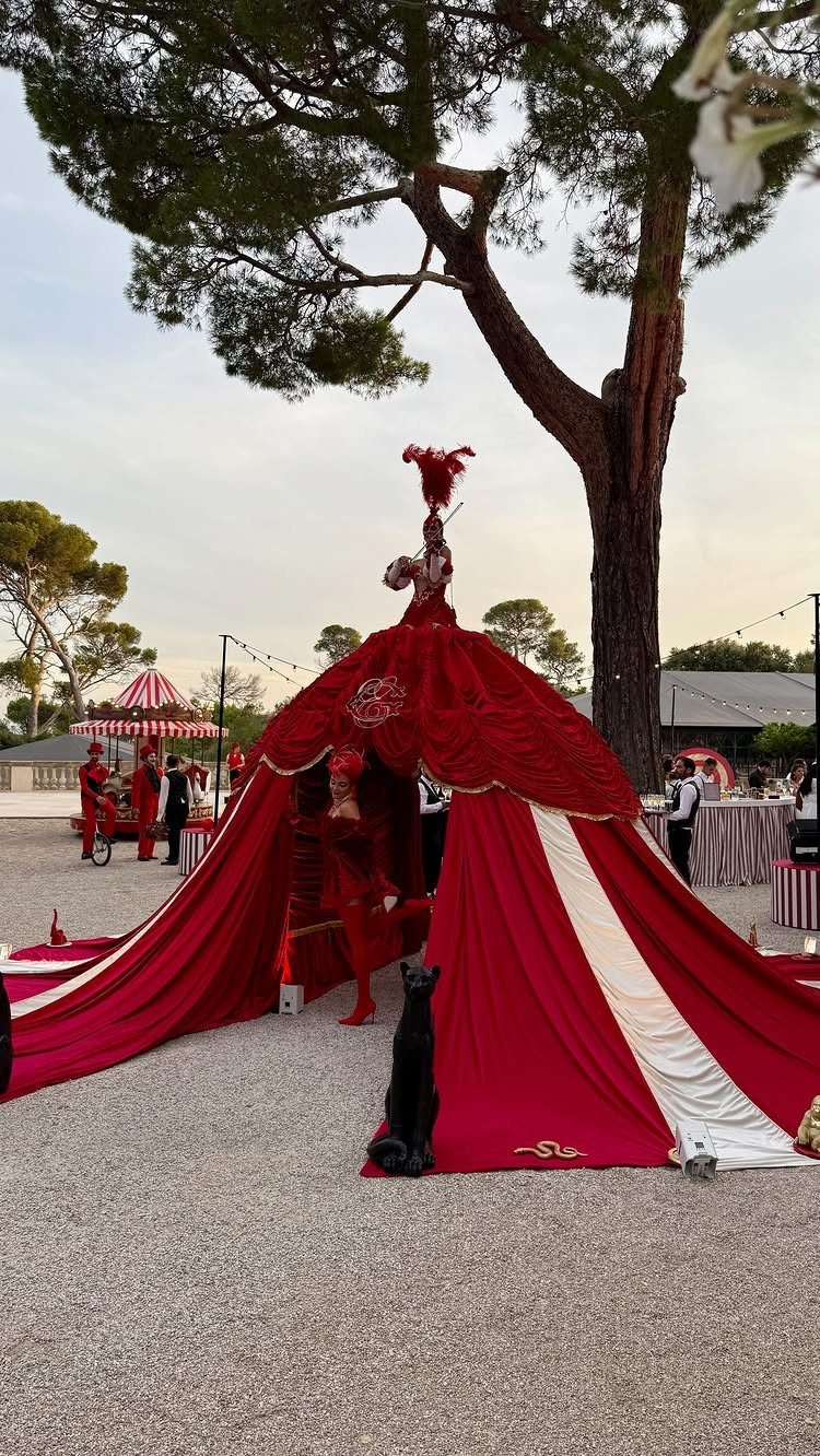 Circus performers in red costumes posing with a large red and white tent structure outdoors.