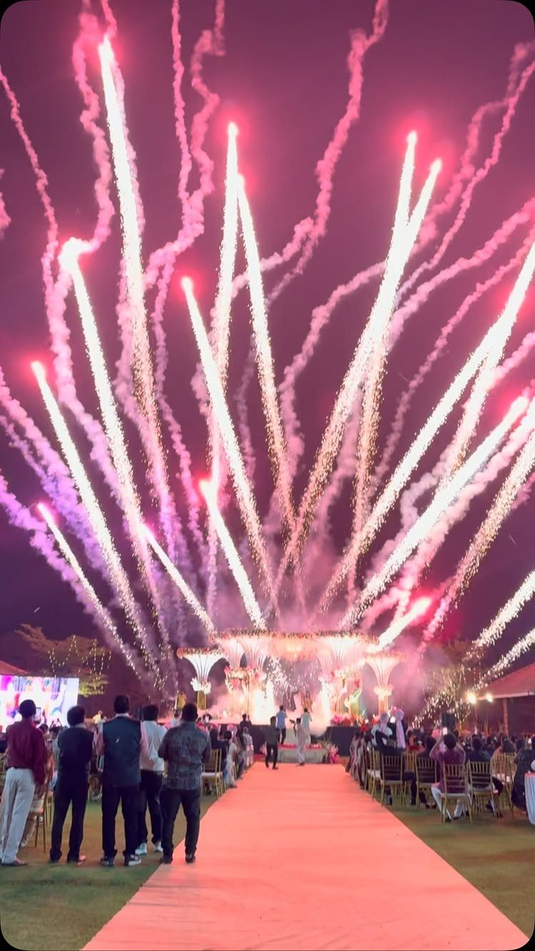 Bright pink and white fireworks shooting into the night sky above a crowd at an outdoor event.