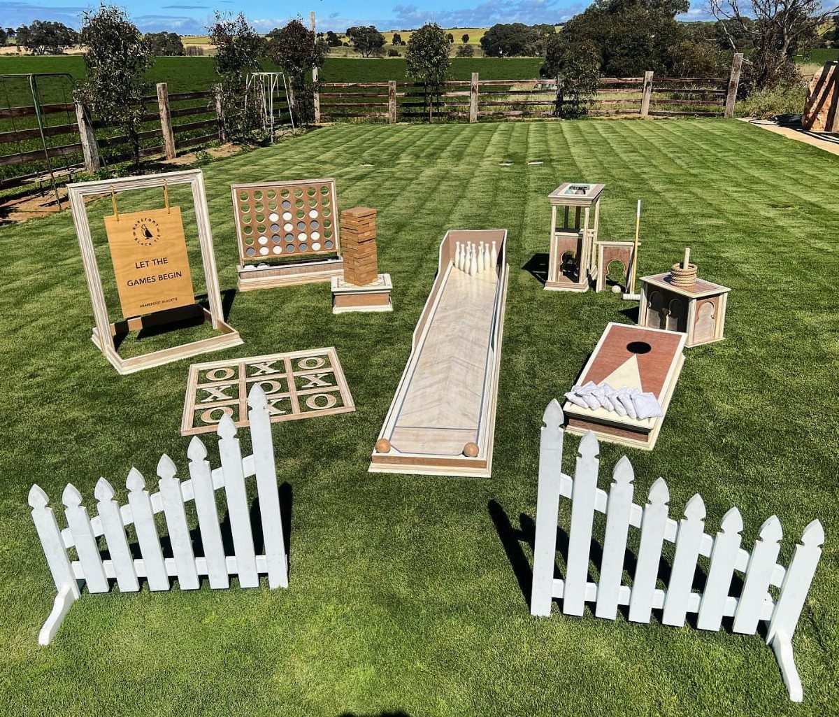 Wooden lawn games arranged on a green grass field behind a small white picket fence.