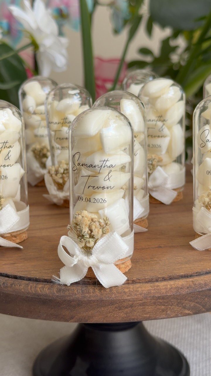 Small glass cloches filled with white candies and decorated with white ribbons on a wooden stand.