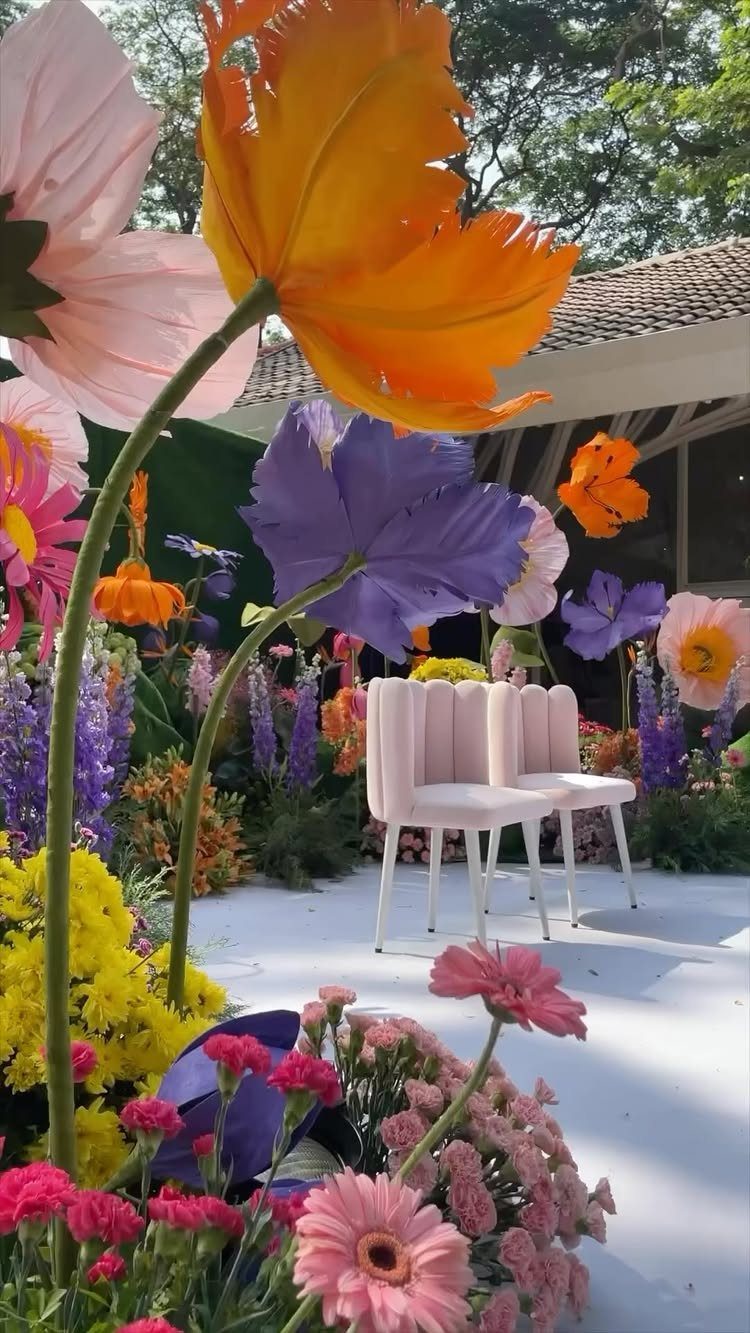 Three pink scalloped velvet chairs sitting among large colorful flowers in a garden setting.