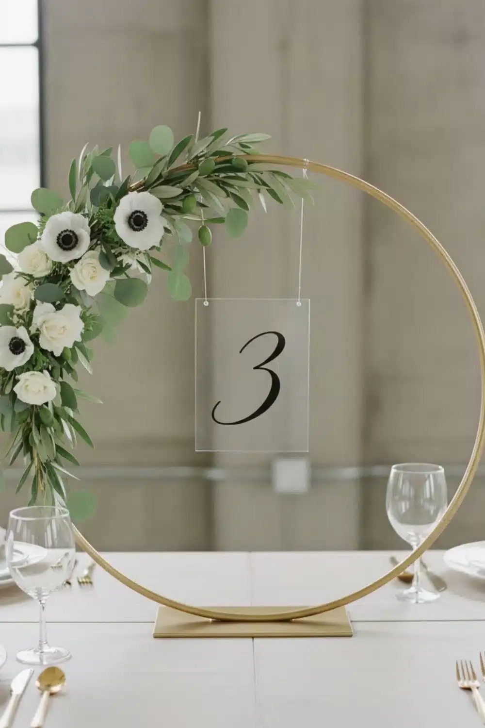 8 Dollar Tree Wedding Decor 2 A gold metal hoop decorated with white flowers and greenery holding a clear table number sign.
