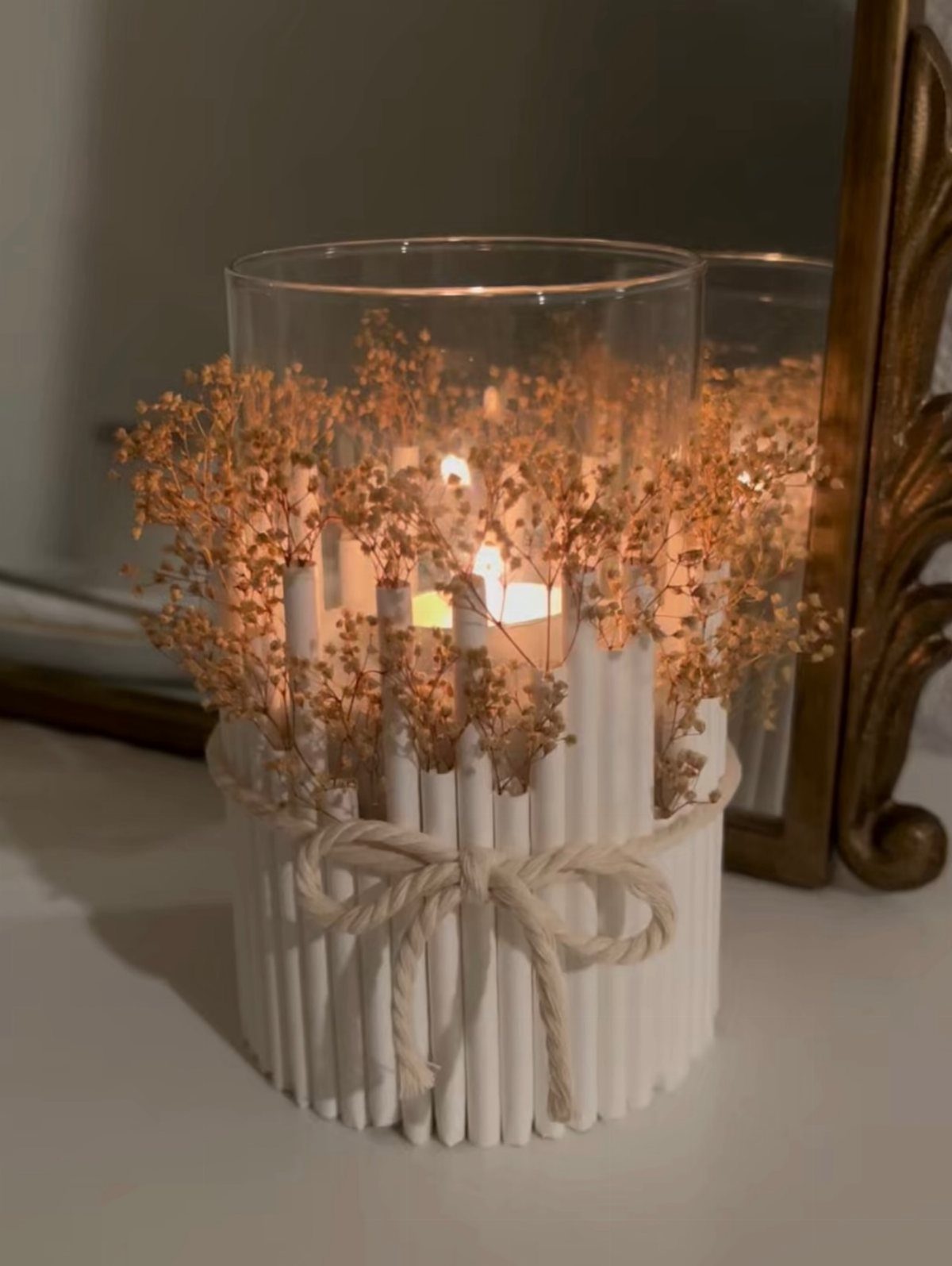 8 Dollar Tree Wedding Decor 8 A glass cylinder vase decorated with white sticks, rope, and dried flowers containing a lit candle.