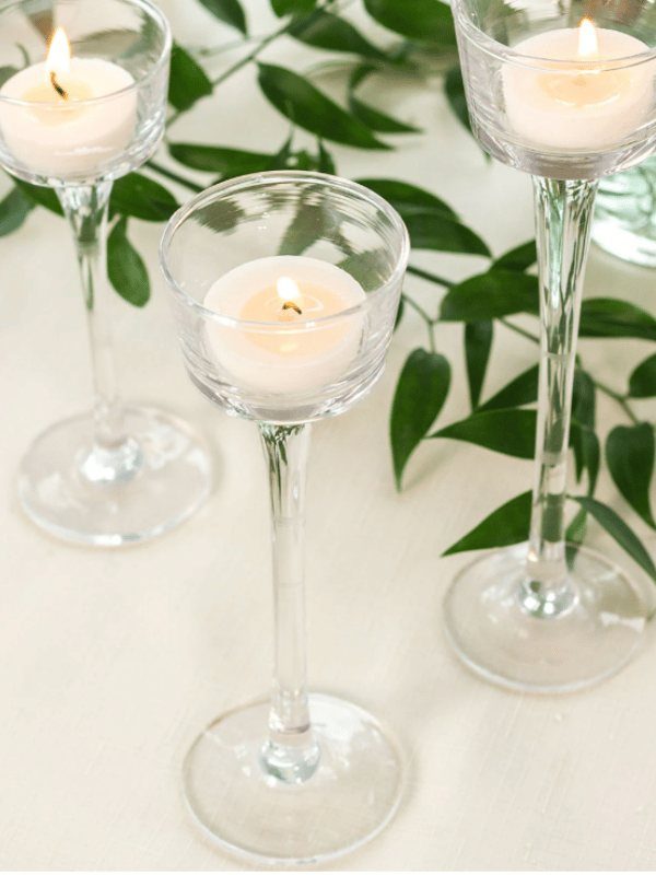 8 Dollar Tree Wedding Decor 7 Three lit tea light candles in tall, clear glass stemmed holders among green leaves.