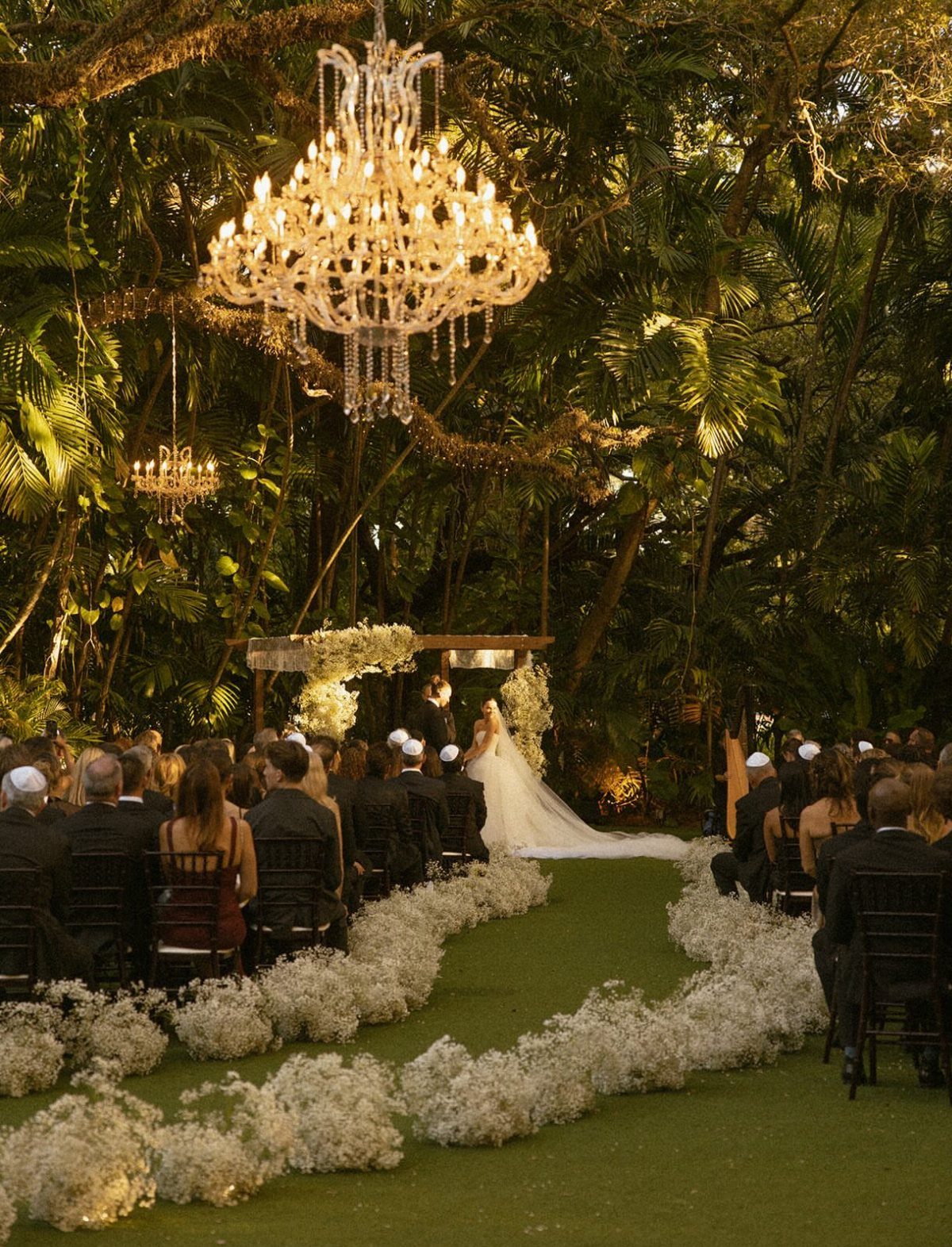 10 Ethereal and Romantic Wedding Ideas That Feel Like a Dream 2 A wedding ceremony set in a lush tropical garden with a large crystal chandelier hanging above.