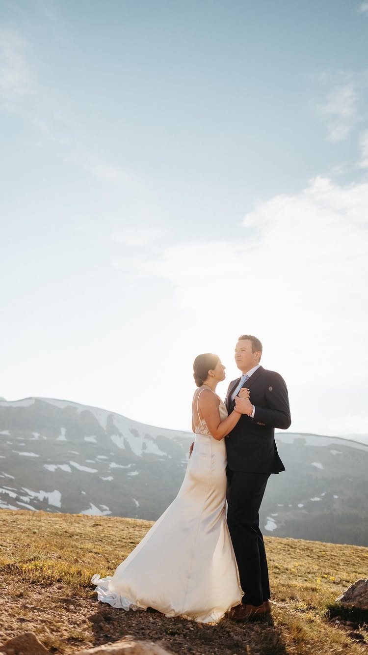 10 Ethereal and Romantic Wedding Ideas That Feel Like a Dream 3 A bride and groom posing together on a mountain ridge under a bright sky.