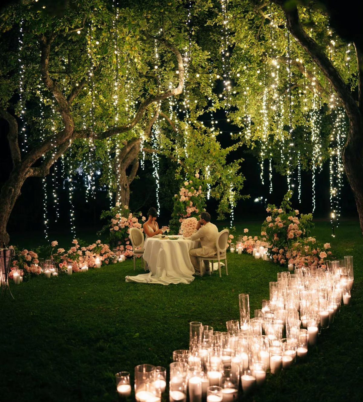 10 Ethereal and Romantic Wedding Ideas That Feel Like a Dream 1 A couple dining under a tree decorated with hanging fairy lights and surrounded by glowing candles.