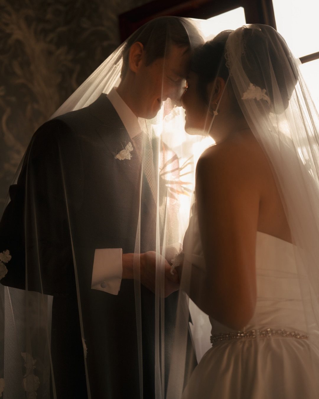 10 Ethereal and Romantic Wedding Ideas That Feel Like a Dream 8 A bride and groom facing each other under a translucent white wedding veil in soft light.