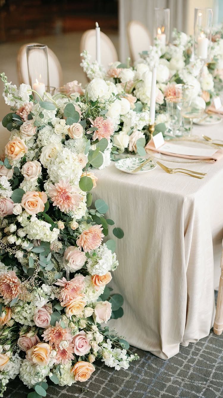 A lush floral garland of white and peach roses cascading down a cream wedding table.