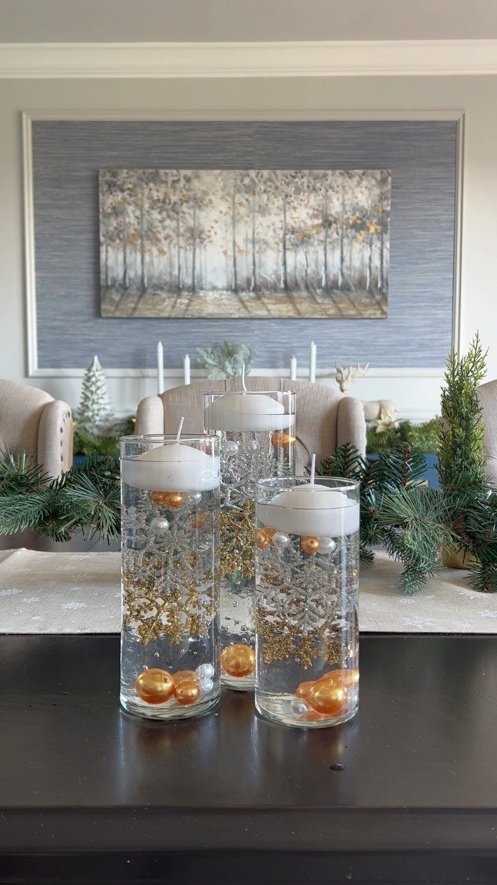 Three glass cylinder vases filled with gold glitter and orange pearls topped with floating candles.