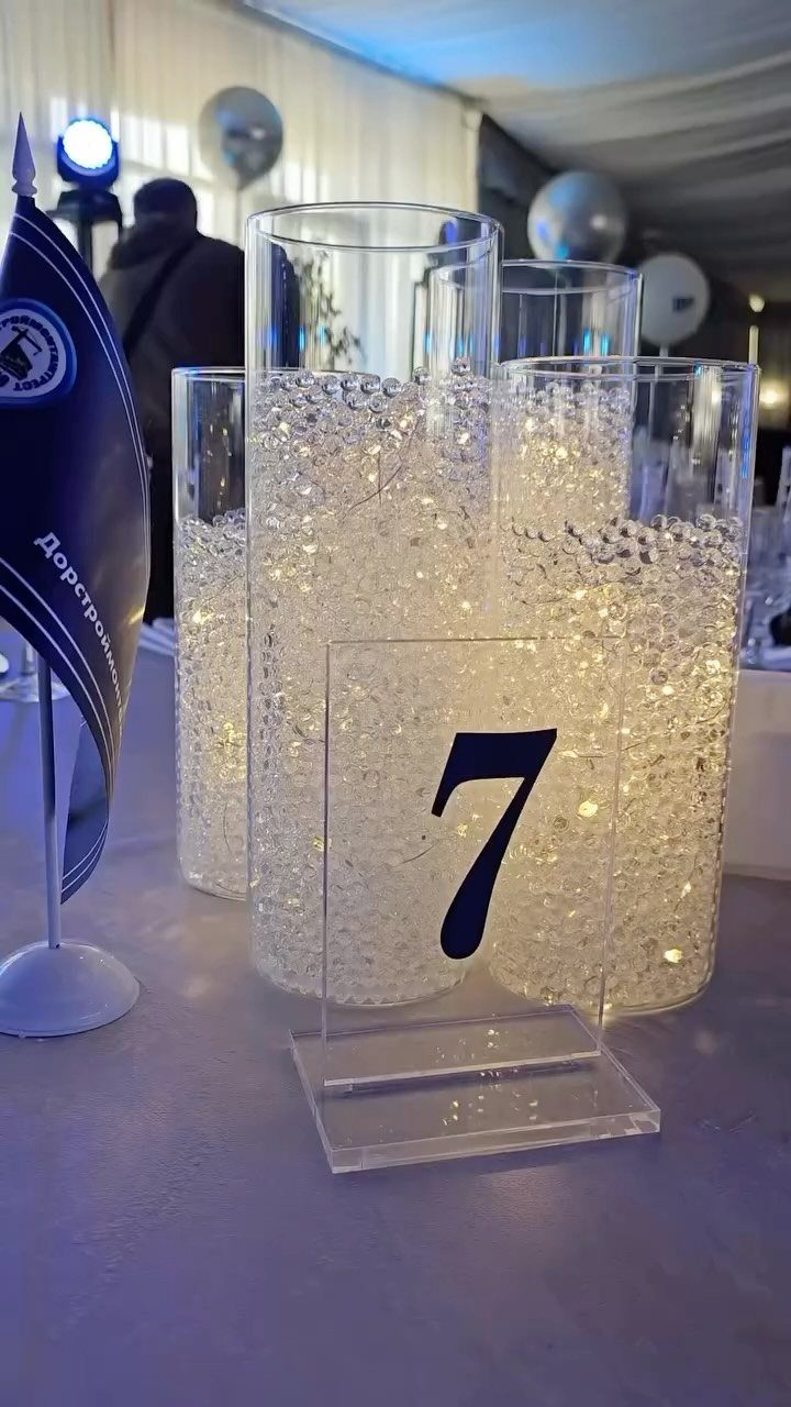 Clear glass cylinder vases filled with glowing submersible fairy lights and small clear beads on a table.
