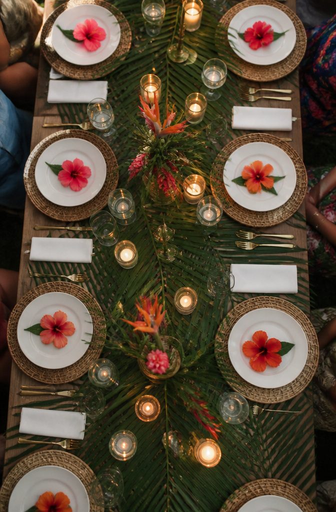A table setting with palm leaves, rattan chargers, and a hibiscus flower.