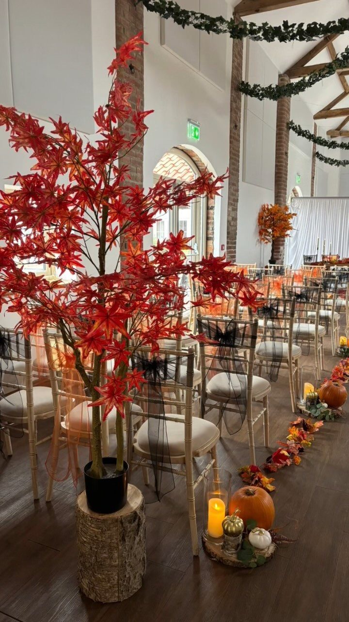 23 Indoor Wedding Decorations for Ceremony and Reception 10 A small artificial tree with bright red maple leaves sits atop a wooden stump indoors.
