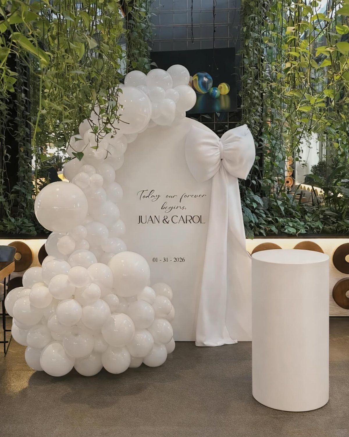 23 Indoor Wedding Decorations for Ceremony and Reception 11 White balloon installation decorating a wedding backdrop with a large fabric bow and printed names.
