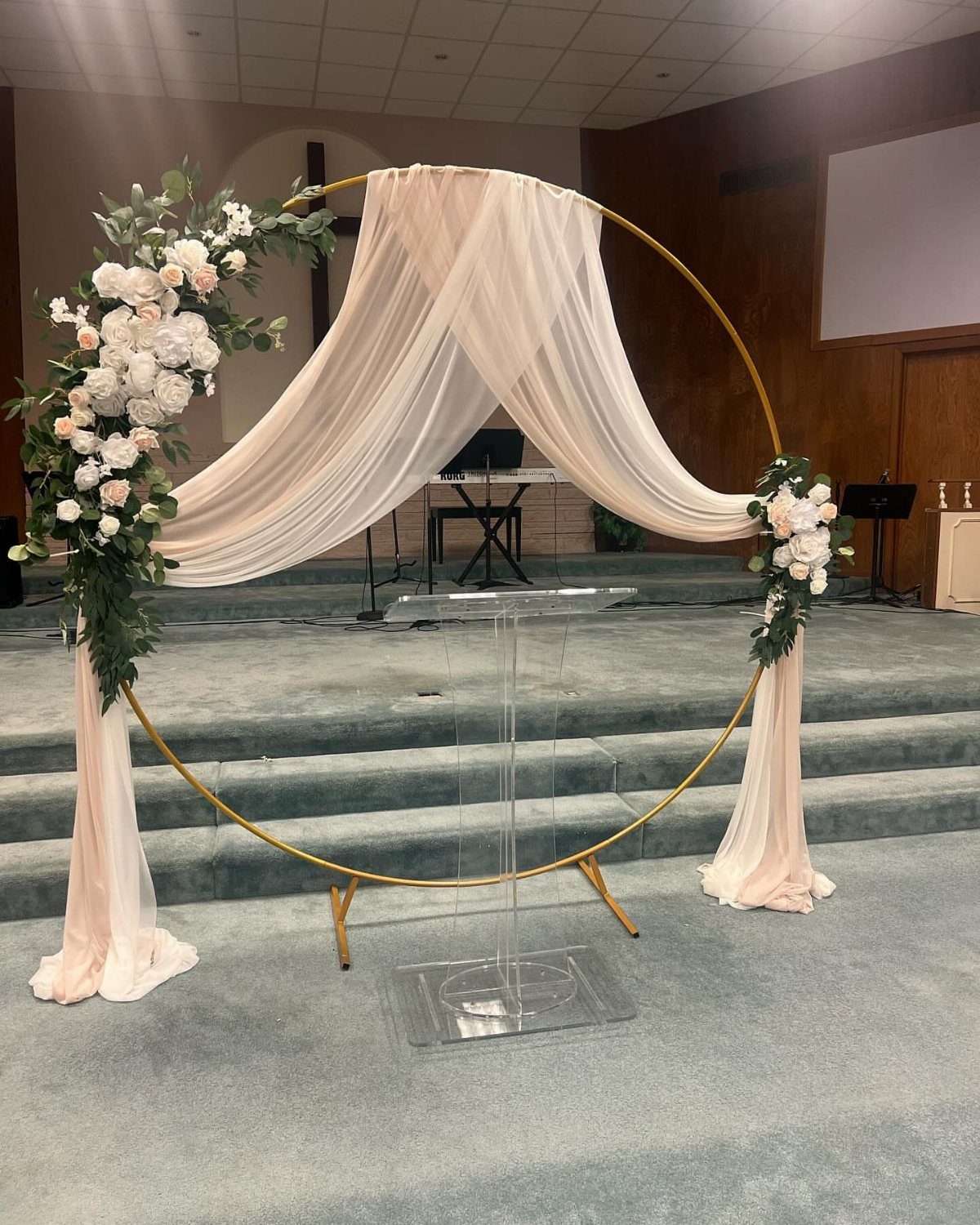 23 Indoor Wedding Decorations for Ceremony and Reception 21 A circular gold wedding arch with peach drapery and white floral arrangements on a stage.