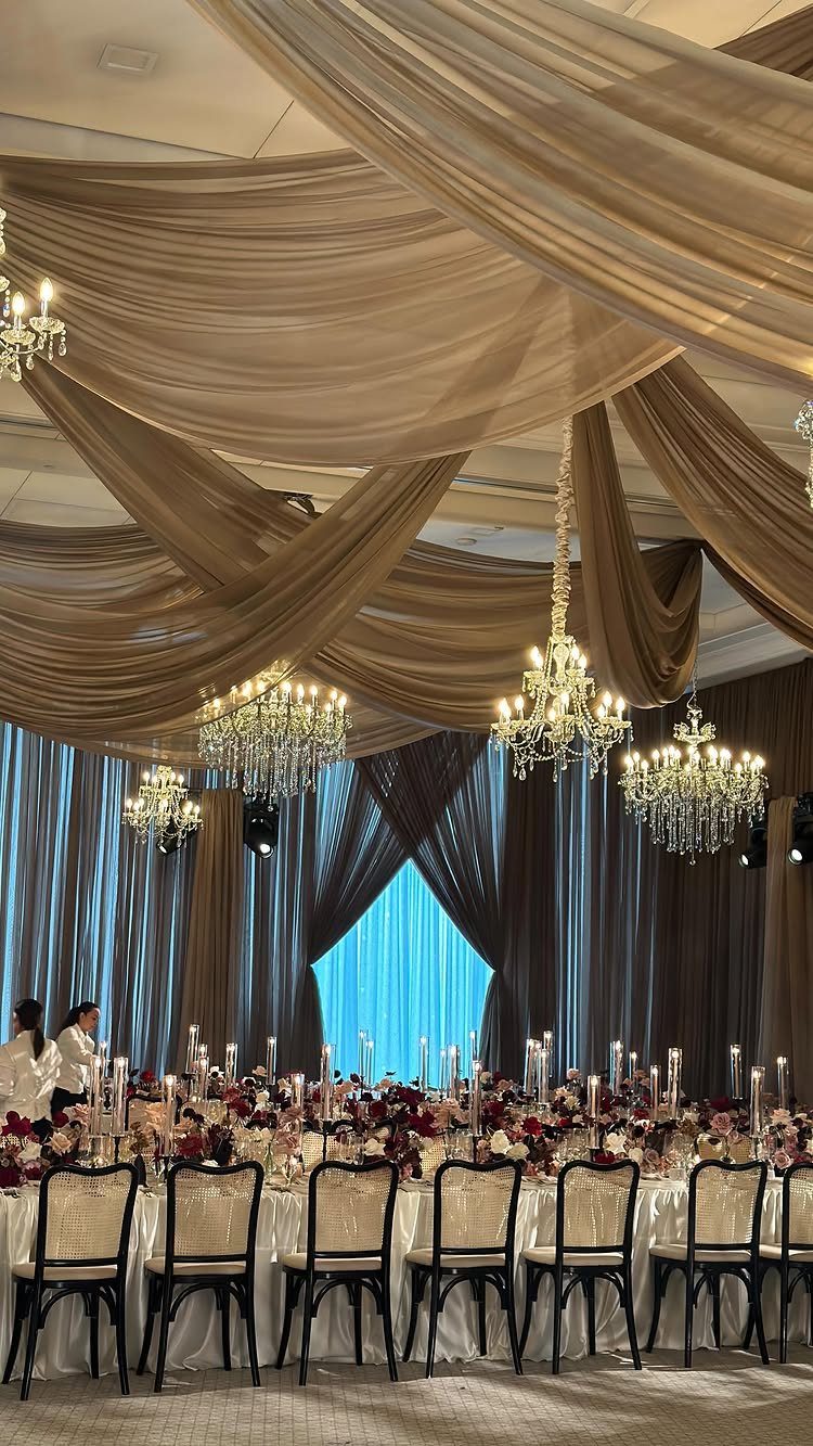 23 Indoor Wedding Decorations for Ceremony and Reception 16 Elegant wedding reception with draped ceiling fabric, crystal chandeliers, and a floral decorated banquet table.