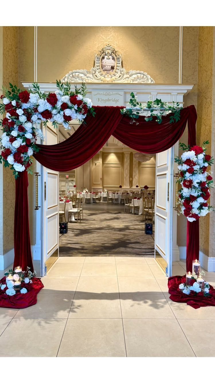 23 Indoor Wedding Decorations for Ceremony and Reception 3 Red fabric draping and red and white floral arrangements decorate a large white doorway entrance.