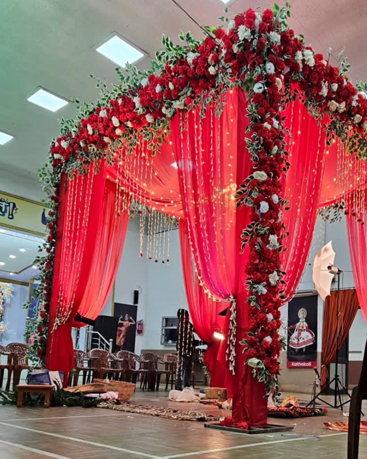 23 Indoor Wedding Decorations for Ceremony and Reception 20 Red fabric canopy decorated with lush red and white rose garlands and green foliage indoors.