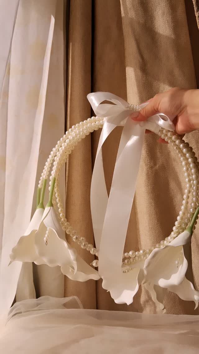 23 Indoor Wedding Decorations for Ceremony and Reception 18 A hand holding a pearl-decorated hoop adorned with white calla lilies and a satin ribbon.