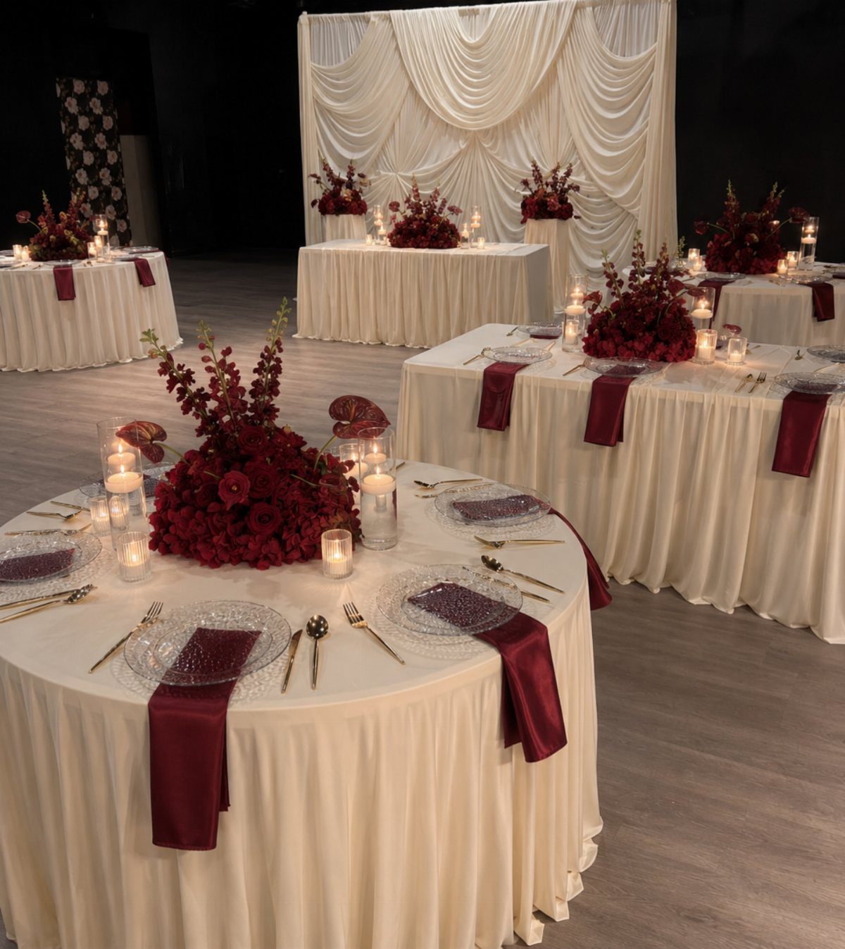 23 Indoor Wedding Decorations for Ceremony and Reception 1 Wedding reception tables featuring cream linens, red floral centerpieces, and burgundy napkins in a dimly lit room.