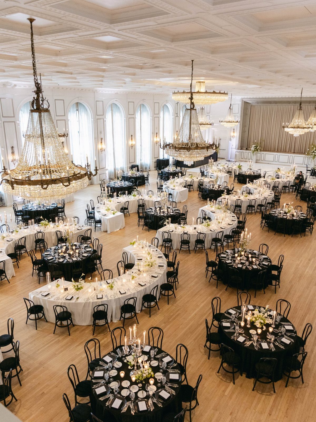 23 Indoor Wedding Decorations for Ceremony and Reception 2 Curved and round banquet tables decorated for a wedding in a grand ballroom with chandeliers.